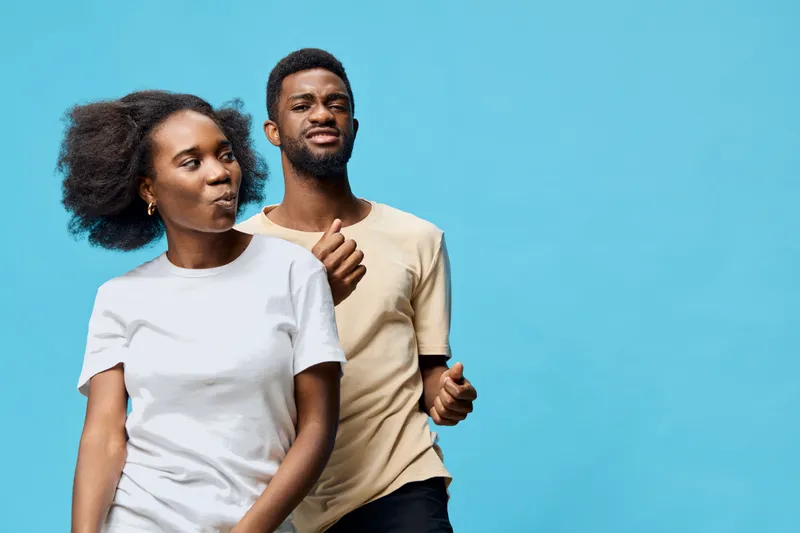 Happy young African couple dancing against a vibrant blue background, wearing casual t shirts, expressing joy and connection through movement and music