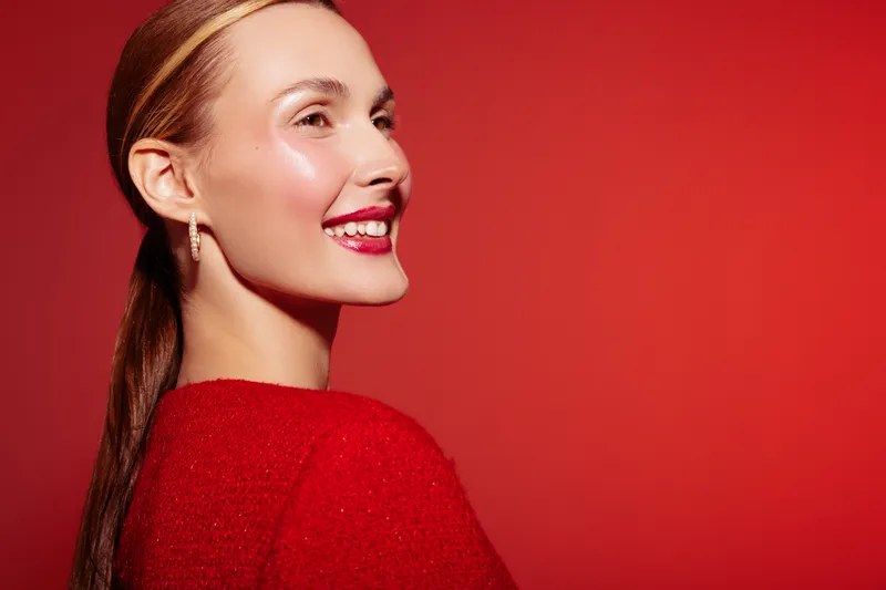 Smiling young woman with red hair and red lipstick wears red sweater against red background. Portrait with natural makeup and joyful expression. Concept of beauty, fashion, and happiness.