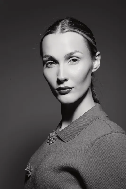 Portrait of a fair skinned Caucasian woman with sleek hair and minimal makeup wearing a textured top. Studio lighting highlights her elegant facial features and confident expression.