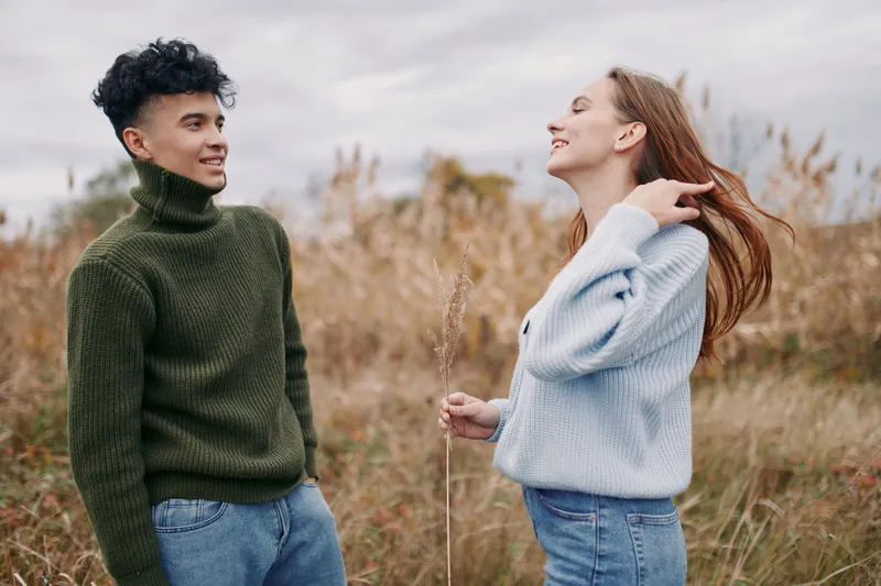 Young couple sharing a genuine outdoor moment in a grassy field, candid interaction and natural smiles conveying authentic connection and believable portrayal of everyday life.