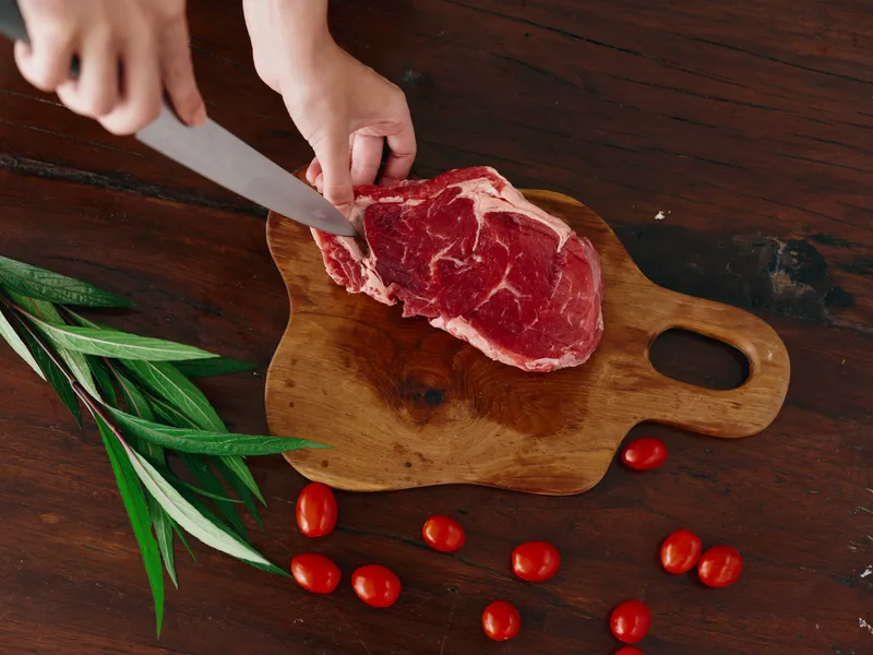 Женщина с ножом в руке нарезает свежее мясо стейка для жарки на кухне