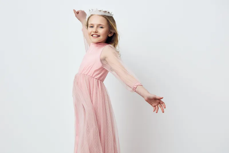 Charming young girl in a pink dress, expressing joy with outstretched arms against a light backdrop, perfect for concepts of happiness and childhood