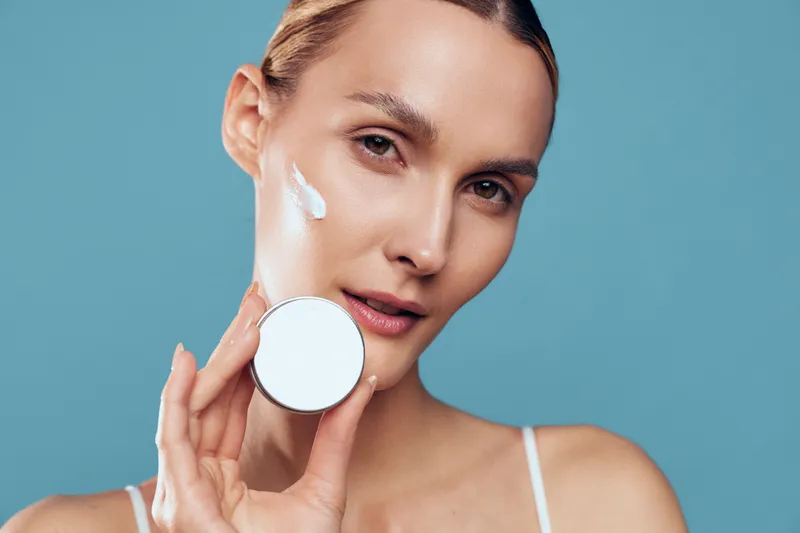 Closeup of a woman, skincare routine, holding cotton pad for hygiene on her face, serum application, smooth cosmetic glow, blue studio background