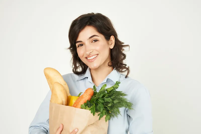 Женщина с пакетом продуктов, овощами, совершает покупки в супермаркете