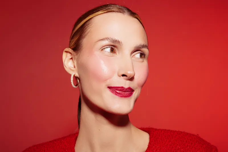 Portrait of a smiling woman with red lipstick and earrings on red background. Concept of beauty, fashion, makeup, and confident female model with natural skin glow and stylish look.