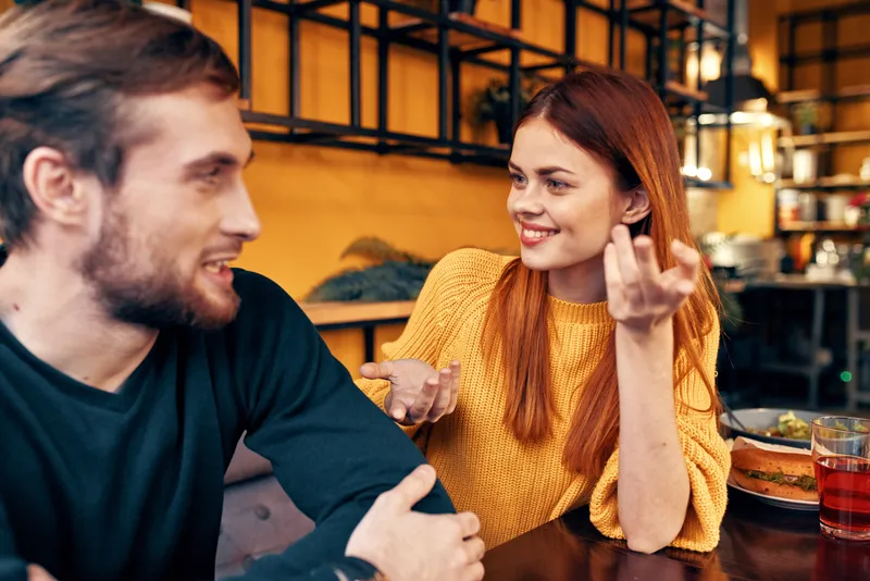 Мужчина и женщина сидят в кафе за столом и жестикулируют руками, друзья, эмоции, веселье, интерьер