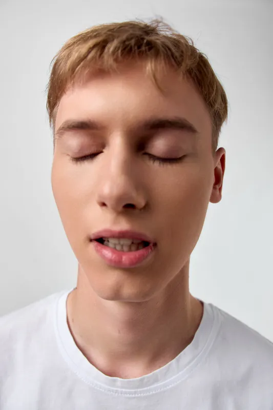Close up of a calm face with eyes closed, light skin, white shirt, soft expression, minimalist background, meditative mood, relaxation and serenity in a simple image