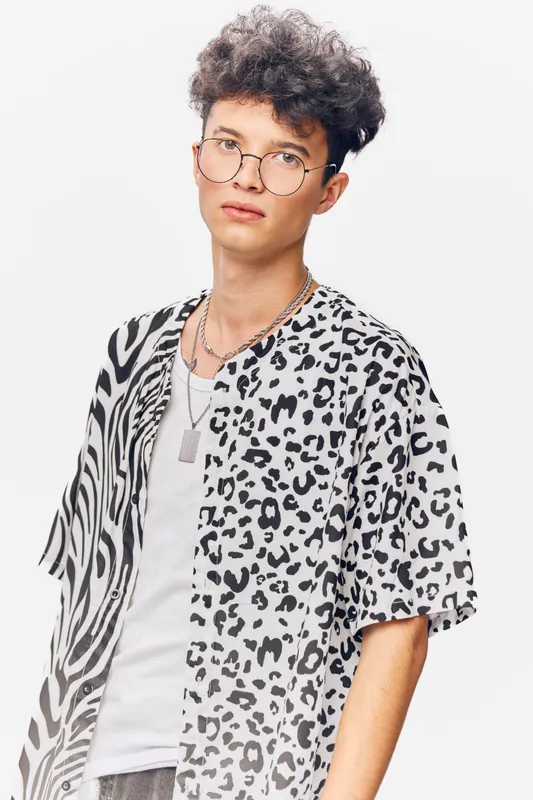 young man wearing animal print shirt and glasses, isolated on white background, casual style and curly hair highlighting modern fashion.