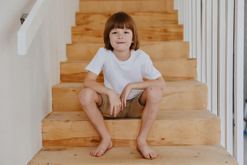 Happy boy sitting on wooden stairs, wearing a white t-shirt and shorts. This image captures a carefree moment of childhood, embodying joy and innocence.