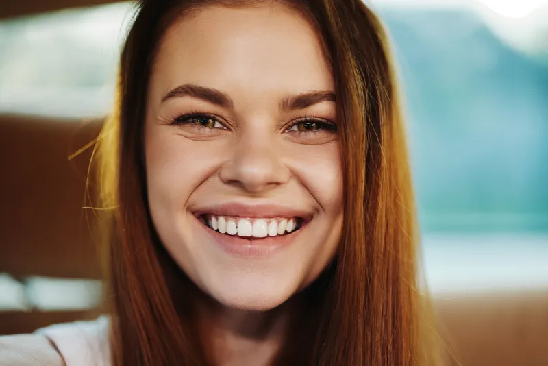 Smiling young woman with long brown hair showcases genuine happiness in a natural setting, highlighting positivity, joy, and beauty.