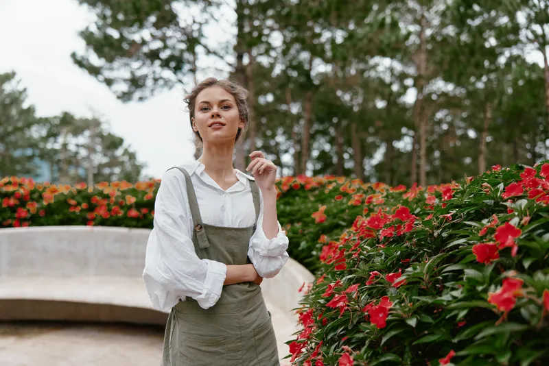 Young woman in a vintage dress standing among vibrant flowers in a serene garden, radiating confidence and peace, perfect for seasonal themes and nature lovers