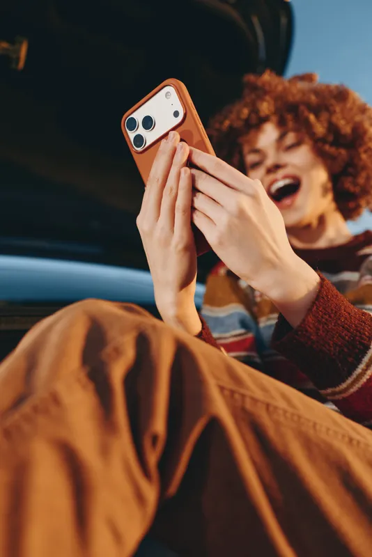 Woman using smartphone with both hands in a car, lifestyle moment of laughing curly hair woman, warm casual lighting, communication call, travel road trip together, friendly self expression