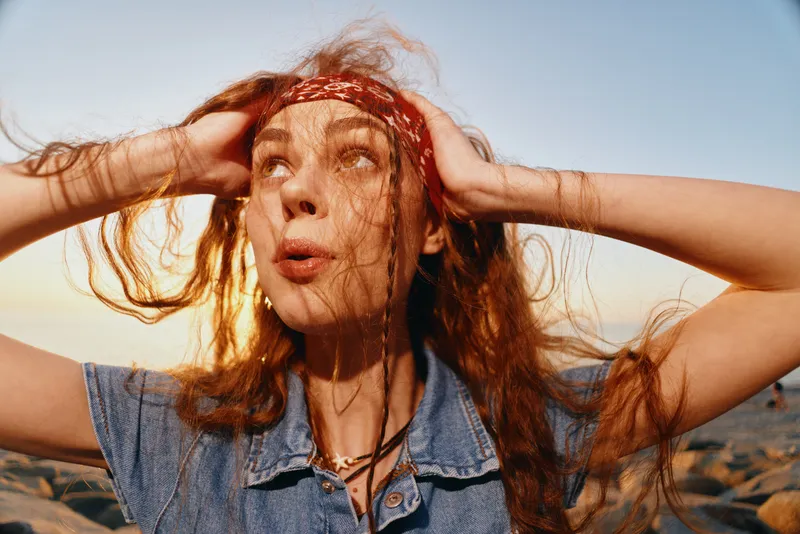 lifestyle woman with modern boho-western denim street style, red hair, bandana, and sunlit film color creating warm and natural outdoor vibe