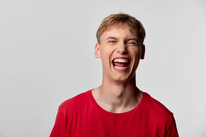 Joyful man laughing with wide open mouth in a red shirt, showcasing energy, happiness, and excitement for celebration, positivity, and upbeat mood in a studio shot