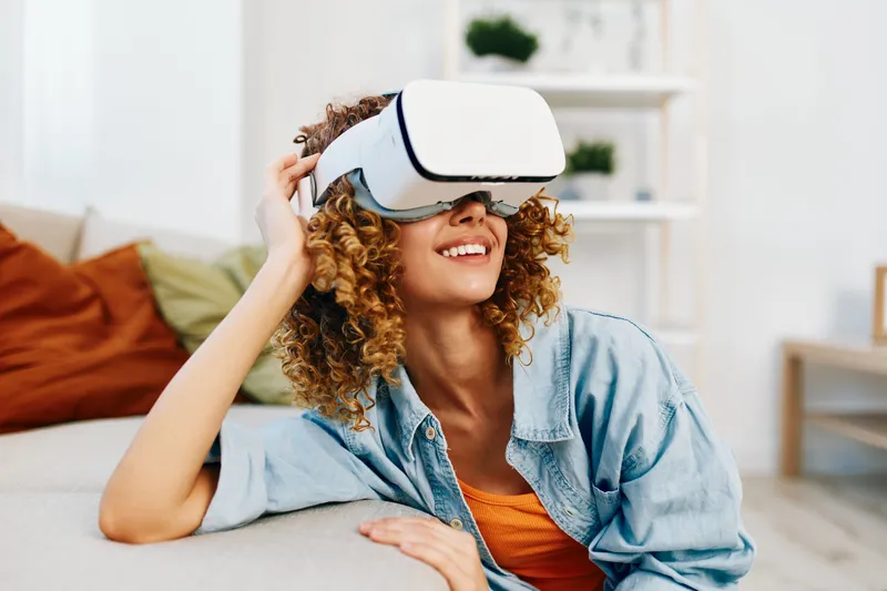 Улыбающаяся женщина наслаждается игрой в виртуальной реальности на диване дома
