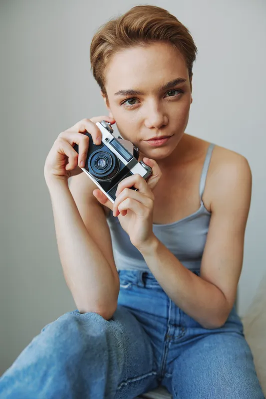 Женщина-фотограф снимает в студии на старую плёночную камеру, сидя дома на диване, портрет на белом фоне, свободное место для копирайтинга, фотограф-фрилансер