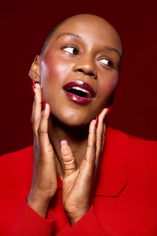 Close-up portrait of a smiling black woman with dark skin wearing red lipstick and red jacket on red background. Concept of beauty, fashion, confidence, and elegance.