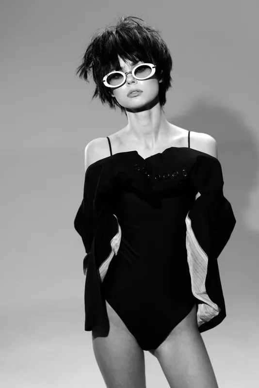 Black and white fashion portrait of stylish woman wearing sunglasses and elegant dress with dramatic pose and modern hairstyle
