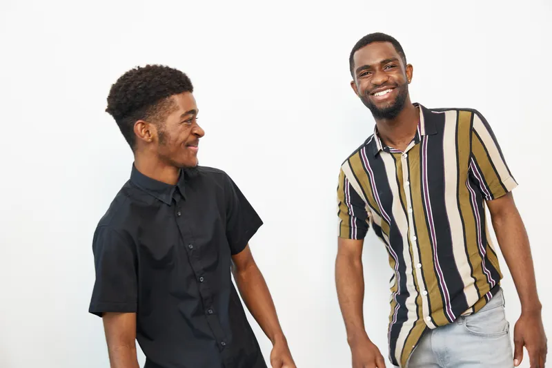 Two smiling African American men in casual attire share a moment of laughter, showcasing joy and camaraderie in a bright, modern setting.