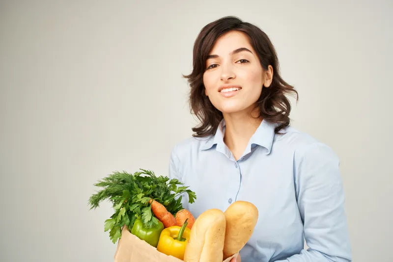 Жизнерадостная женщина с пакетом продуктов, овощей, здоровой еды, доставка еды