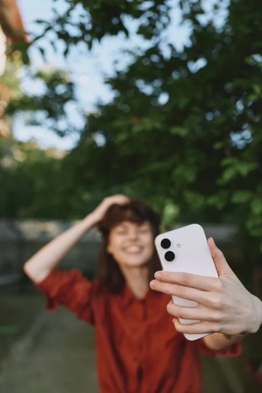 Woman lifestyle selfie outdoors, smiling and relaxed, she takes a casual portrait with a smartphone in a sunny park scene, conveying cheerful everyday moment