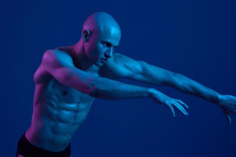 Dynamic man posing in vivid color light, showcasing strength and athleticism while expressing intense emotion in a captivating artistic performance.