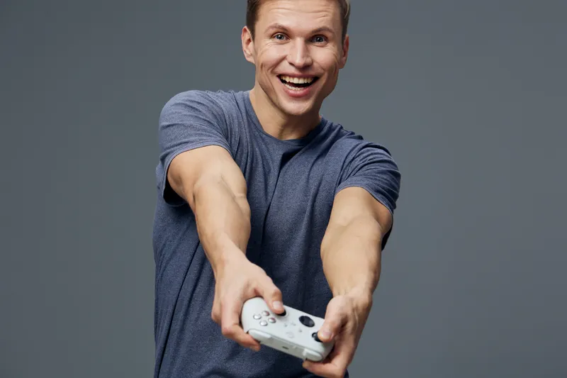 cheerful young caucasian man holding game controller smiling playing video games indoor gray background digital entertainment concept