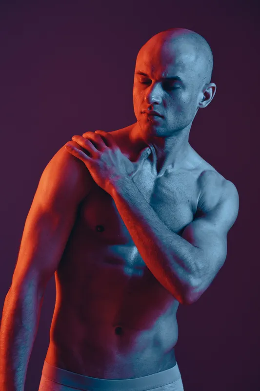 Muscular man with a contemplative expression, showcasing vibrant red and blue lighting, emphasizing his strong physique and emotional depth in a striking composition.