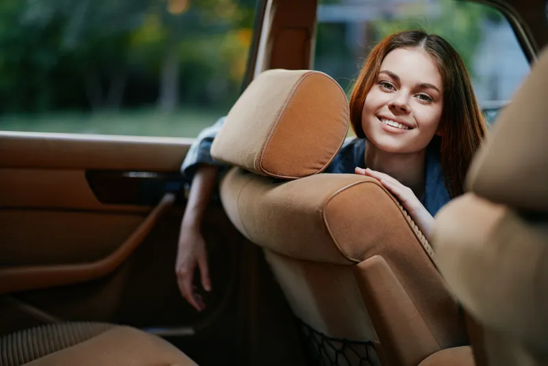 Young woman with long hair smiling in a car, showcasing a relaxed vibe in warm tones, perfect for lifestyle and travel concepts.