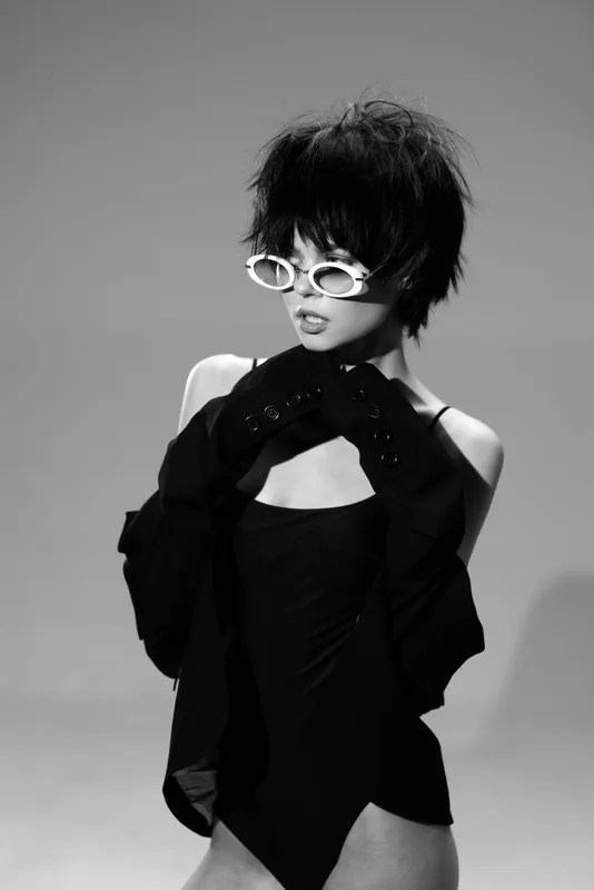 Black and white portrait of a stylish woman wearing sunglasses and gloves, exuding confidence and modern fashion vibes.