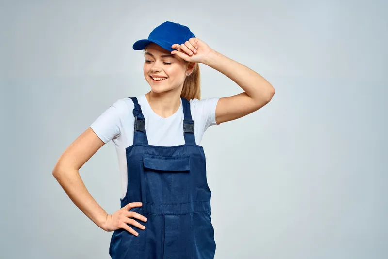 Женщина в рабочей форме, синей кепке, занимается доставкой на светлом фоне