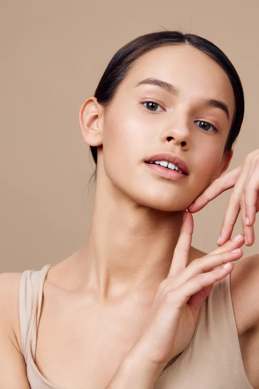 Portrait of a young model with natural beauty, wearing a light, neutral toned top, showcasing a serene expression against a minimalistic beige background