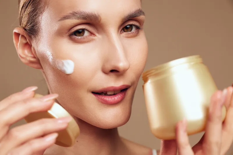 woman skincare cream jar face beauty hydration wellness cosmetic treatment concept, close up of a woman applying facial cream from a jar, smooth cheek texture under soft studio light, calm beauty