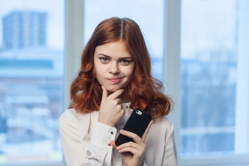 Деловая женщина в белой рубашке с телефоном в руках общается