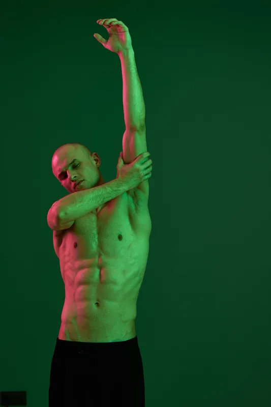 Athletic man stretching against a green backdrop, showcasing his muscular physique and flexibility. A vibrant, artistic portrayal capturing the essence of movement and energy.