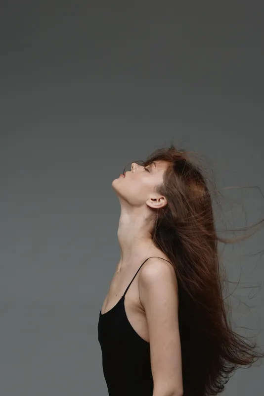 Young woman in black dress with long hair looking upwards against gray background, contemplative mood, minimalistic style