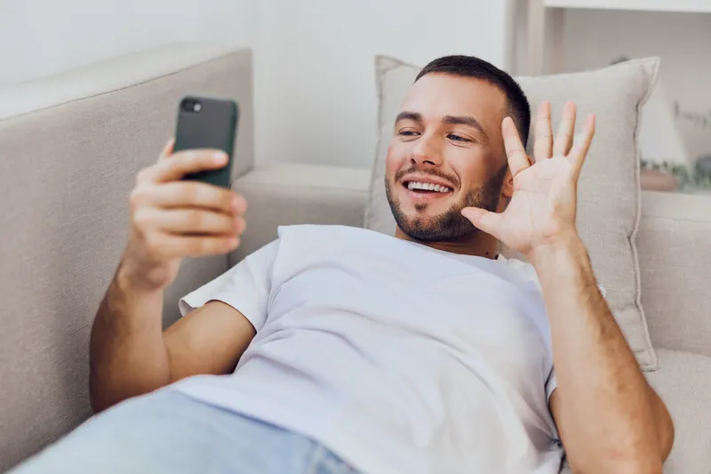 Happy man using smartphone while relaxing on the couch, capturing a joyful moment. Inspired by contemporary lifestyle trends and digital communication.