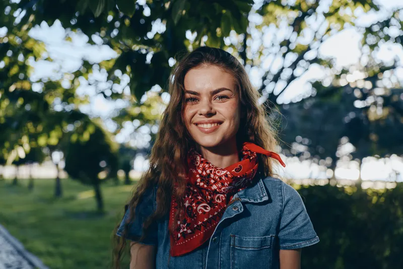 lifestyle woman with modern boho-western denim outfit and red bandana smiling outdoors in natural sunlight, film color style, casual street fashion vibe