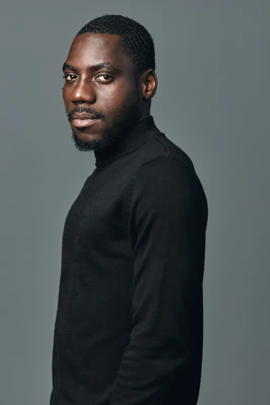 African man portrait in creative conceptual visual style wearing black sweater looking at camera with confident expression on gray background in studio lighting setup.