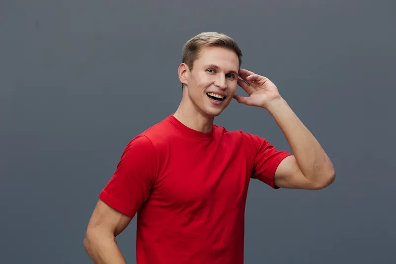 Smiling happy young man with short brown hair wearing red t-shirt looking at camera isolated on plain gray background studio portrait. People lifestyle concept