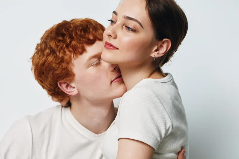 Young couple with affectionate pose, man kissing woman on neck while embracing. Intimate moment with love, tenderness and connection between two people in casual clothes.