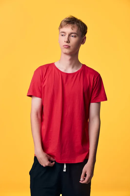 Red t shirt worn by casual man against a bright yellow backdrop, minimalist studio shot showing relaxed pose and simple fashion style