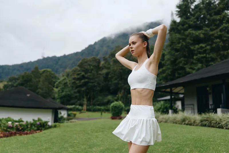 Beautiful young athletic woman in white sportswear enjoying outdoor fitness, surrounded by nature in a lush green landscape