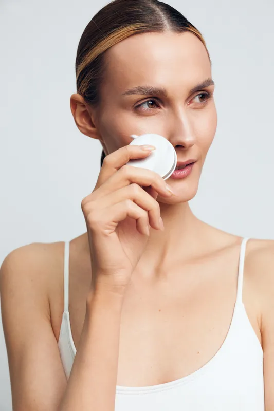 Woman skincare and spa beauty portrait, cream care, holding a small cup to her face, fresh clean look, relaxed expression, soft light, smooth skin, minimal studio calm background