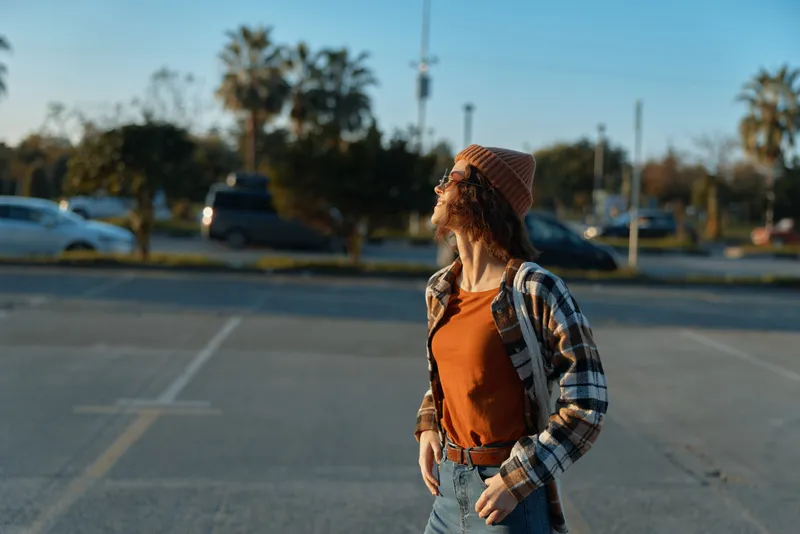 Woman portrait, candid moment in an urban parking lot at golden hour, beanie and plaid shirt, relaxed pose capturing authenticity, candid lifestyle, golden hour glow and emotional storytelling.
