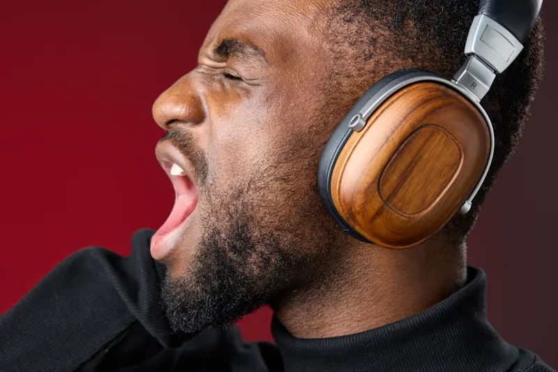 Young African man passionately singing while wearing wooden headphones against a red background, expressing joy and musical enthusiasm