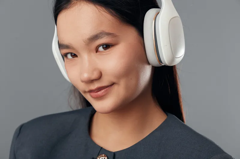 Young woman with headphones smiling closeup portrait on gray background, casual style, listening to music or podcast, technology and lifestyle with natural expression.