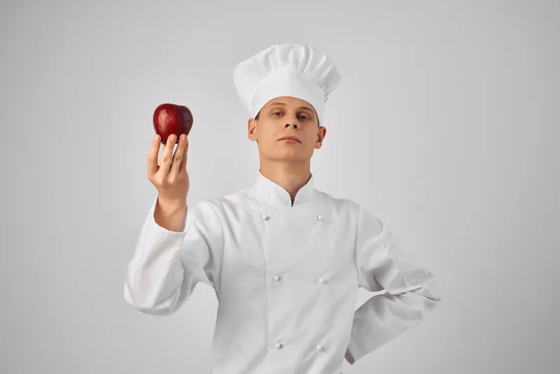 Шеф-повар с яблоком в руке, свежие продукты на профессиональной кухне