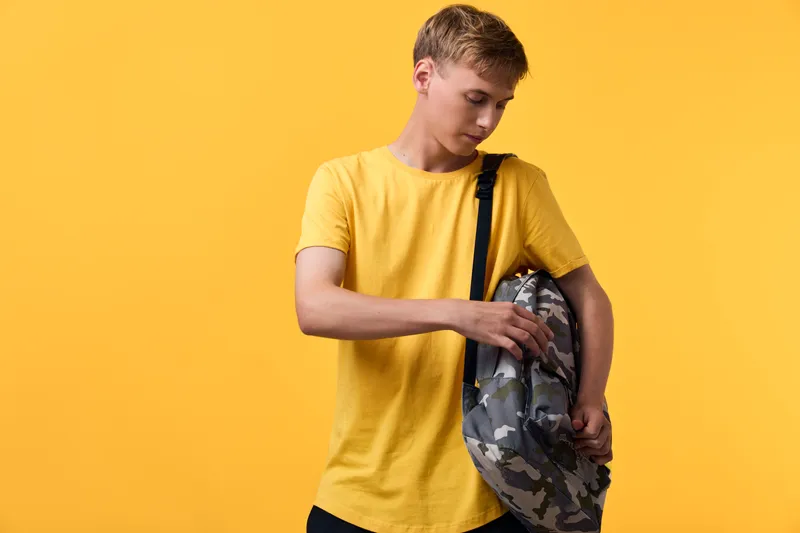 Young youth with a camouflage backpack on a bright yellow backdrop, casual top, exploring travel gear and streetwear style, ready for school or an outdoor adventure