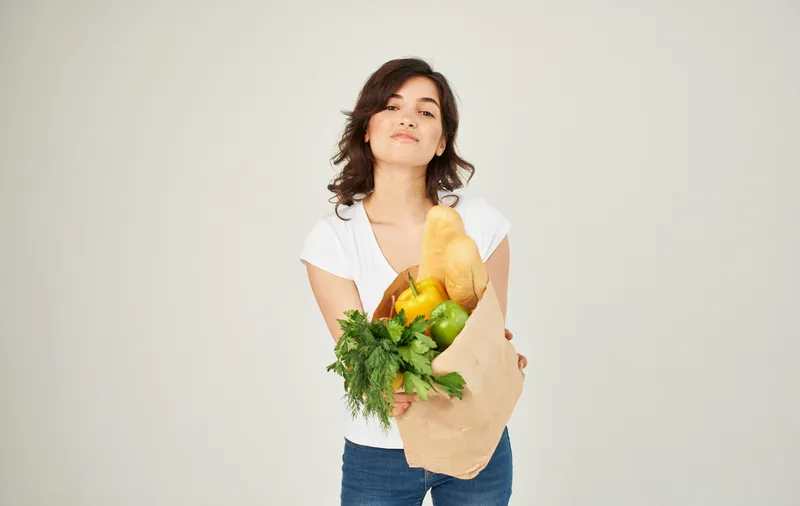 Весёлая женщина с пакетом продуктов из супермаркета, совершающая покупки здоровой пищи